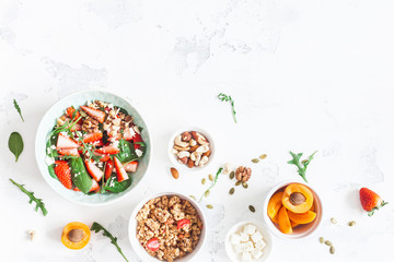 Breakfast with muesli, strawberry salad, fresh fruit, nuts on white background. Healthy food...