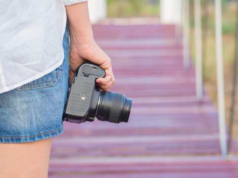 Asian Woman wearing white shirt and hold the camera, Standing on a wooden bridge, On a sunny days.