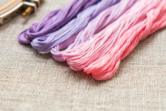 Set for embroidery. Embroidery thread shades of violet and pink color on linen homespun cloth. Coloring and processing photos. Shallow depth of field.