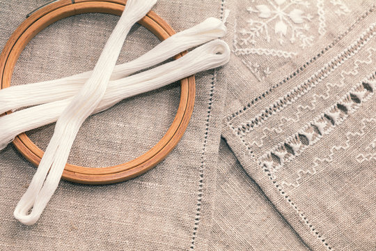 Set for embroidery. Embroidery thread white color, embroidery hoop and needle on linen with needlework in progress. Coloring and processing photos. Shallow depth of field.
