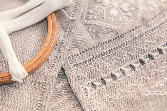 Set for embroidery. Embroidery thread white color, embroidery hoop and needle on linen with needlework in progress. Coloring and processing photos. Shallow depth of field.