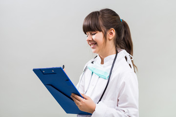 Beautiful little doctor writing on clipboard.