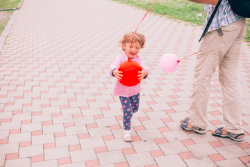 Happy little girl playing with colorful toy balloons outdoors.