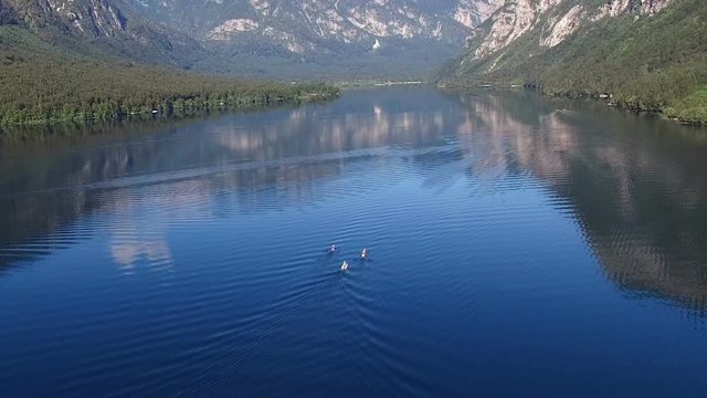 Flight above amazing Bohinj Lake in the morning. People are training in rowing. Blue deep water and Julian Alps mountains. Triglav National Park, Slovenia, Europe.