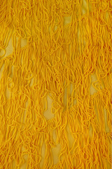 Yellow fabric with thread fringes. Material with fringes background top view.