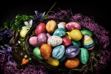 Easter Basket Chocolate Bunny. Easter basket with colored eggs and chocolate Easter bunny on table with colorful grass and flowers.