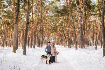 Fototapeta na wymiar Outdoor happy couple in love posing with dog in cold winter weather. Young boy and girl having fun outdoor. Boho