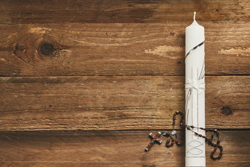 White Eucharist candle and rosary on wood