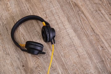 Headphones with yellow cable. Modern device for listening music. Sound earphones lying on wooden rustic background.