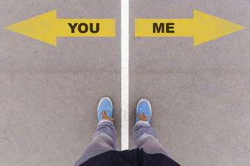 You or Me text arrows on asphalt ground, feet and shoes on floor
