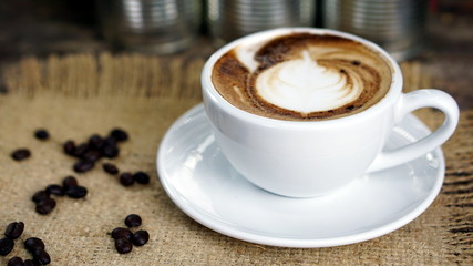 Cappuccino coffee. A cup of latte, cappuccino or espresso coffee with milk put on a wood table with dark roasting coffee beans. Drawing the foam milk on top.