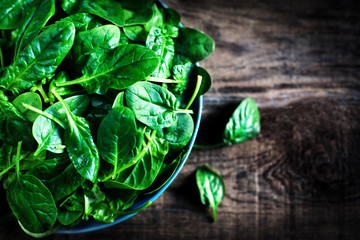 Fresh green baby spinach leaves  in a bowl on a rustic wooden ta