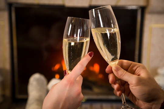 Closeup of couple's hands with glass of champagne near fireplace