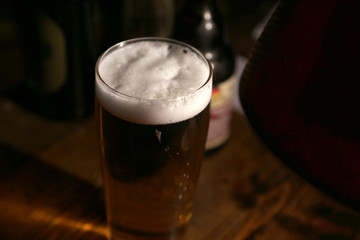bier im glas in einer kneipe und bierflaschen im hintergrund