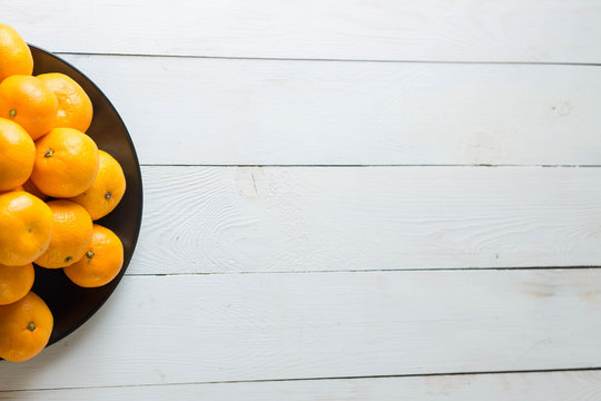 ripe delicious yummy bright tangerines on black plate on white wooden background with space for inscriptions horizontal