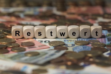 restwert - Holzwürfel mit Buchstaben im Hintergrund mit Geld, Geldscheine
