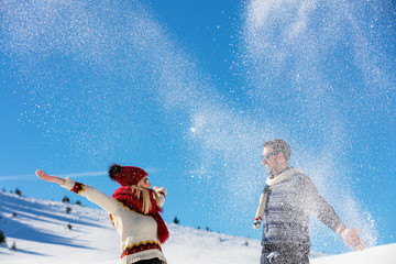 Snowball fight. Winter couple having fun playing in snow outdoors. Young joyful happy multi-racial...