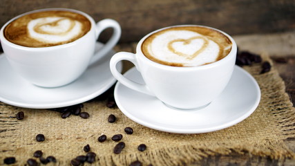 Cappuccino coffee. A cup of latte, cappuccino or espresso coffee with milk put on a wood table with dark roasting coffee beans. Drawing the foam milk on top.
