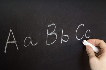Teacher is writing letter of alphabet on blackboard with chalk. Education in elementary school concept.