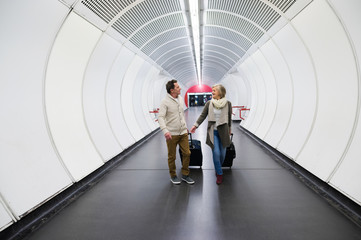 Senior couple in hallway of subway pulling trolley luggage.
