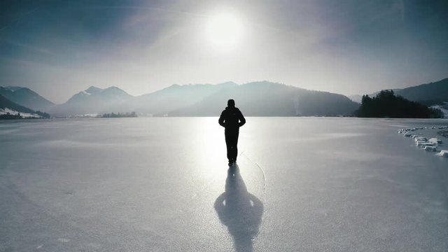 Lonesome man walking on frozen lake schliersee, bavaria, germany, near munich against mountains.
