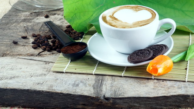 Cappuccino coffee and chocolate cookies. A cup of latte, cappuccino or espresso coffee with milk put on a wood table with dark roasting coffee beans and cookies. Drawing the foam milk on top.