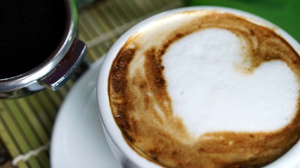Cappuccino coffee. A cup of latte, cappuccino or espresso coffee with milk put on a wood table with dark roasting coffee beans. Drawing the foam milk on top.