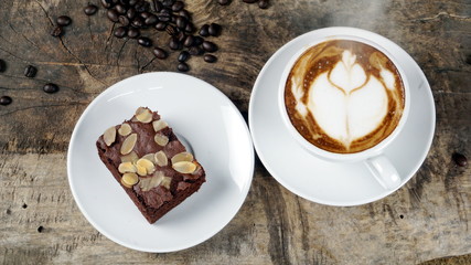 Cappuccino coffee and sweet chocolate brownies cake. A cup of latte, cappuccino or espresso coffee with milk put on a wood table with dark roasting coffee beans. Drawing the foam milk on top.
