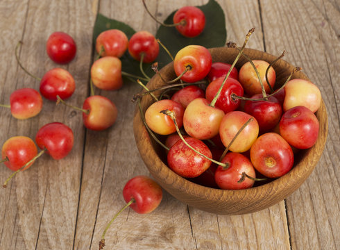 Background of ripe cherries. Pile of fresh and tasty cherries in wooden bowl. Fresh cherries scattered on a wooden table. Top view.