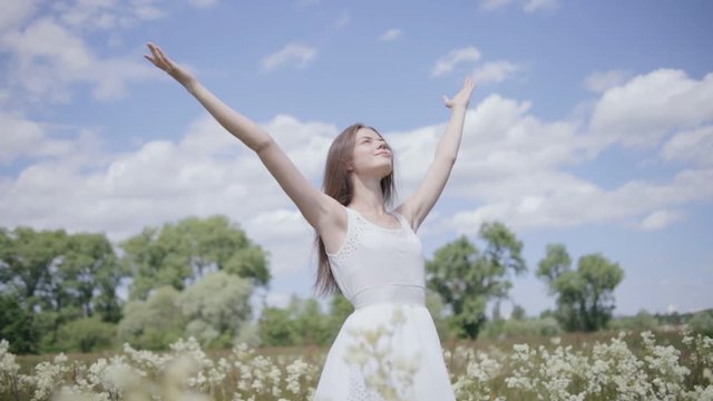 Young pretty woman in the middle of flower meadow with spreaded hands