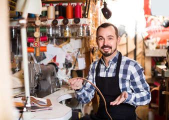 male worker sewing stitches on belt in leather workshop