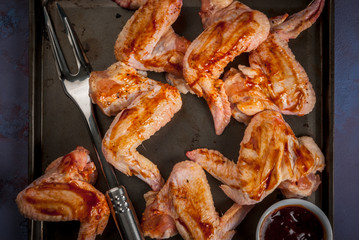 Ready for roasting barbecue wings baffulo - with barbecue sauce and spices, fork for meat on cutting board on the stone black concrete gray table. Top view, copy space