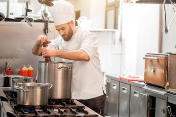 Chef cook in uniform peppering soup in the big cooker at the restaurant kitchen