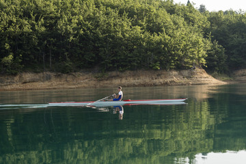 A Young single scull rowing competitor paddles on the tranquil lake