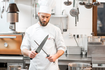 Portrait of chef cook in uniform with knifes at the restaurant kitchen