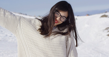 Happy young woman wearing spectacles in snowy landscape with raised arm