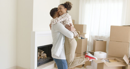 Joyful young couple celebrating their move to a new home hugging and laughing in front of stacked boxes
