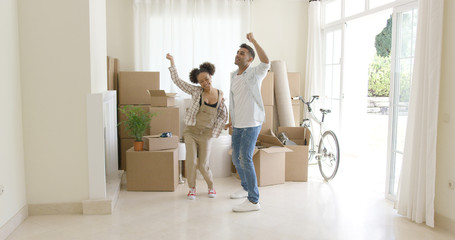 Young couple dancing for joy in the living room of their new home with packing boxes behind them