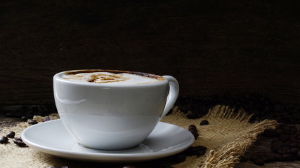Cappuccino coffee with love and hearts. A cup of latte, cappuccino or espresso coffee with milk put on a wood table with dark roasting coffee beans. Drawing the foam milk on top.