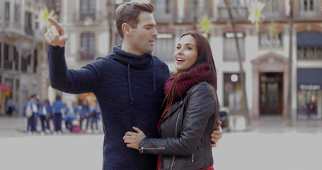 Attractive young man pointing out something in an urban square to his smiling girlfriend or wife  close up head and shoulders