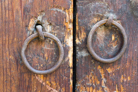 Two rusty iron ring door knobs over an old wooden door
