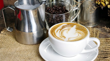 Cappuccino coffee. A cup of latte, cappuccino or espresso coffee with milk put on a wood table with dark roasting coffee beans. Drawing the foam milk on top.