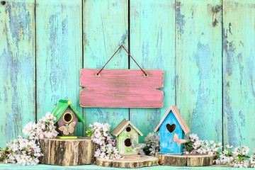Blank pink wood sign hanging over colorful birdhouses with spring flowers