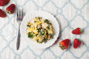 Potato Spinach Egg Scrambler on white and blue place mat with strawberries horizontal shot