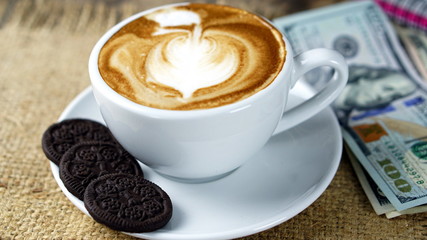 Cappuccino coffee and sweet chocolate brownies cake. A cup of latte, cappuccino or espresso coffee with milk put on a wood table with dark roasting coffee beans and US bills money.