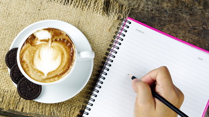 Cappuccino coffee and sweet chocolate brownies cake. A cup of latte, cappuccino or espresso coffee with milk put on a wood table with dark roasting coffee beans. and memo notebook.