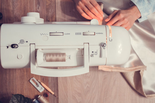 top view of the hand of a girl who is sewing at the sewing machine, see the desktop and the fabric