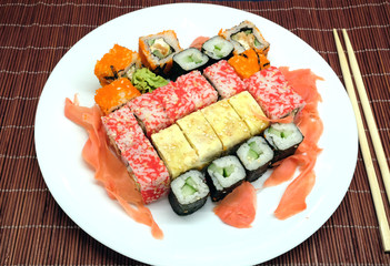 Sushi pieces on white plate and two chopsticks over brown wicker straw mat top view closeup