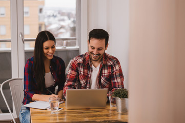 Happy beautiful couple using laptop together sitting at the table