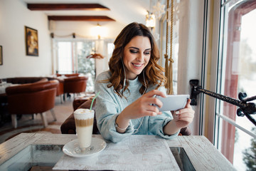 Happy woman with curls in cafe using smart phone and smiling